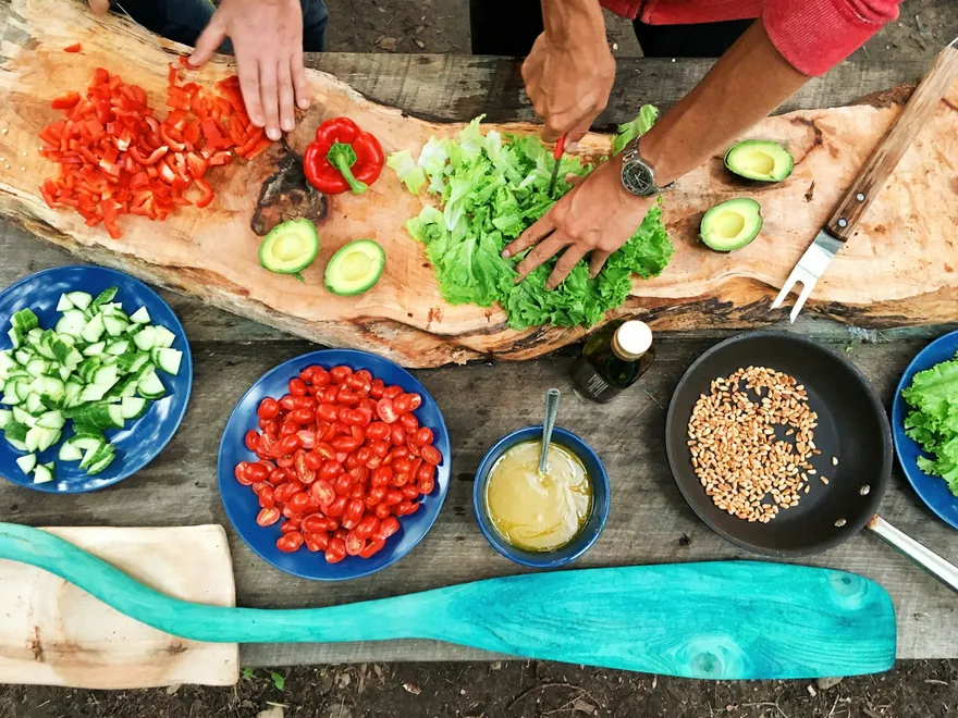 Plusieurs mains coupent des légumes sur une grande planche en bois pendant un atelier de cuisine